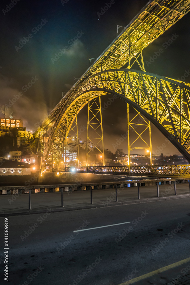 Obraz premium road and old metal arch bridge in the rays of spotlights against the night sky and luminous houses