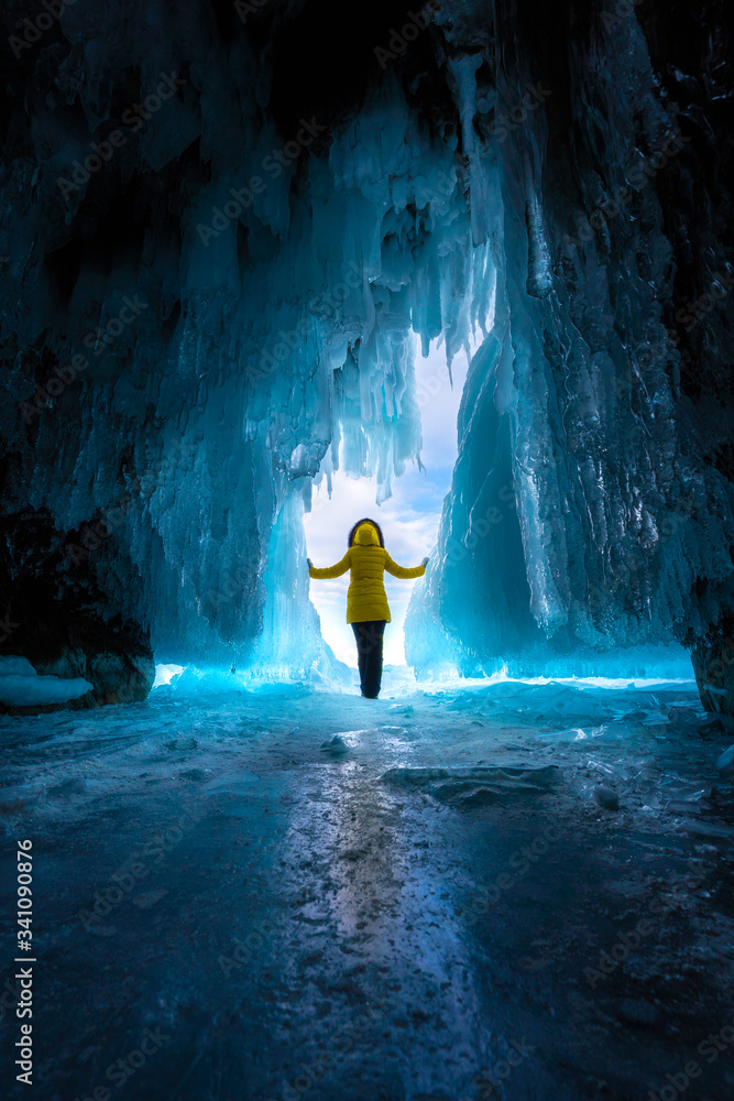 Fototapeta premium a girl in a yellow jacket stands at the exit of an ice cave in bright light