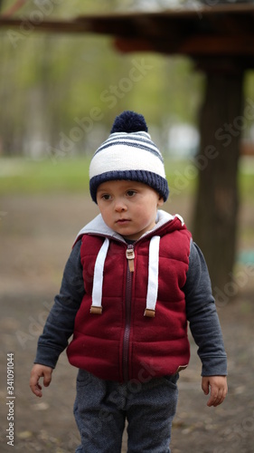 Portrait of little cute boy in red jacket and white-blue hat in spring in park © www.akolosov.art 