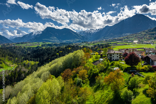 Aerial view of valley Cares, Trentino, green slopes of the mountains of Italy, huge clouds over a valley, roof tops of houses, Dolomites on background, bridges, river and roads, spring colors photo