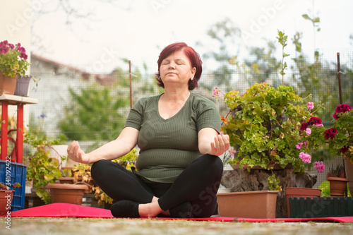 Mature beautiful woman doing yoga in the garden of her house. The woman who is at home in quarantine has a good time at home by doing sports.
