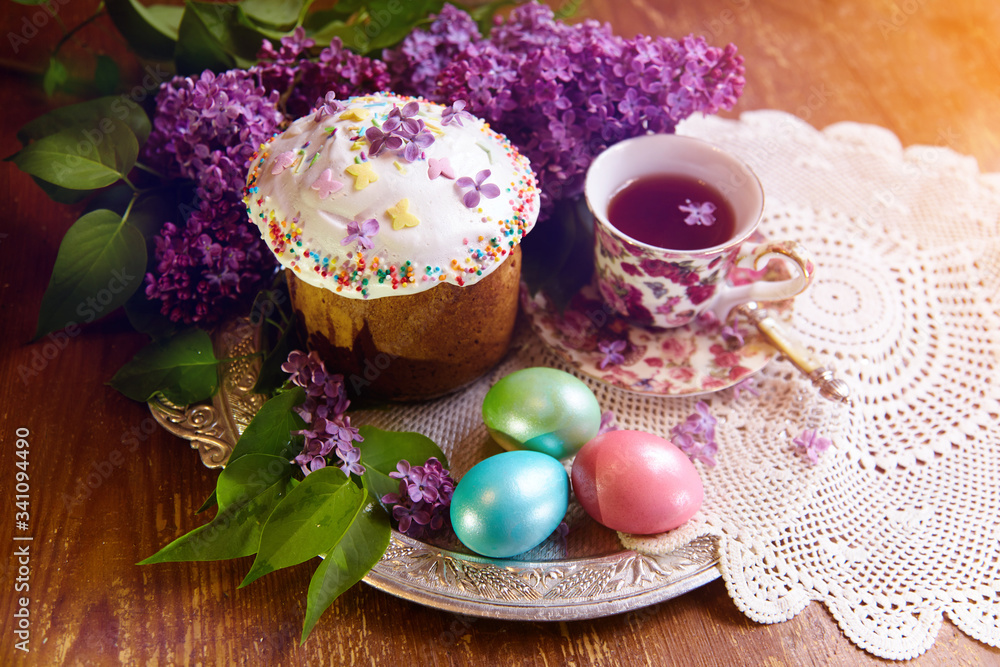 The Easter cake is on a tray on an old wooden table. The cake is smeared with white whipped sugar and sprinkle with colored sprinkles next to one egg.
