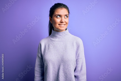 Young beautiful woman with blue eyes wearing casual turtleneck sweater over pink background looking away to side with smile on face, natural expression. Laughing confident.