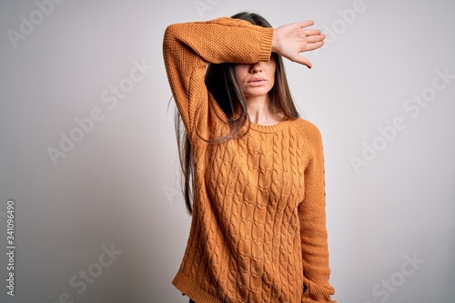 Young beautiful woman with blue eyes wearing casual sweater standing over white background covering eyes with arm, looking serious and sad. Sightless, hiding and rejection concept
