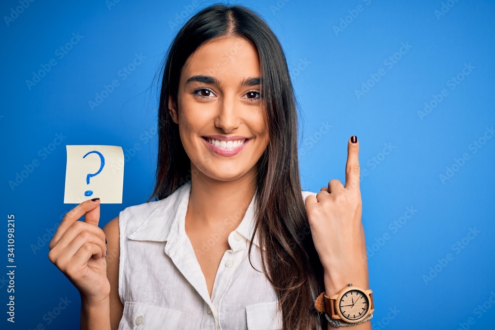 Question Pointing Young beautiful brunette woman holding paper with question mark symbol ...