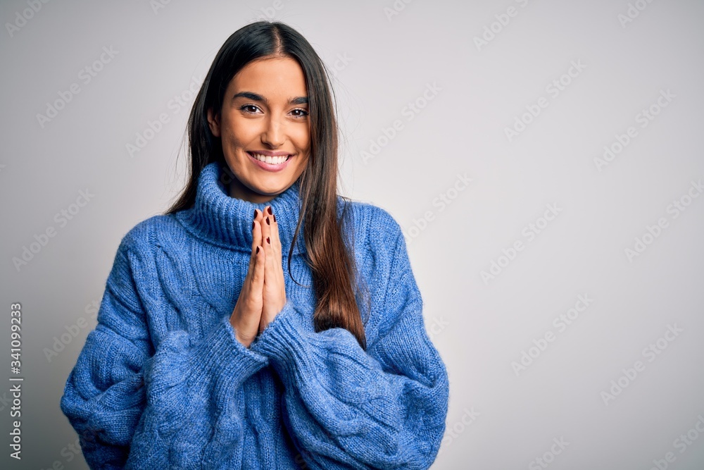 Young beautiful brunette woman wearing casual turtleneck sweater over white background praying with hands together asking for forgiveness smiling confident. Young beautiful brunette woman wearing casual turtleneck sweater over white background praying with hands together asking for forgiveness smiling confident.