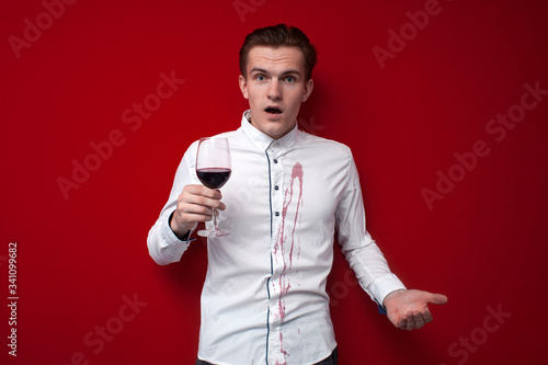 sad guy in a white shirt spilled red wine on himself on a red background, an angry man put a stain of wine on his clothes