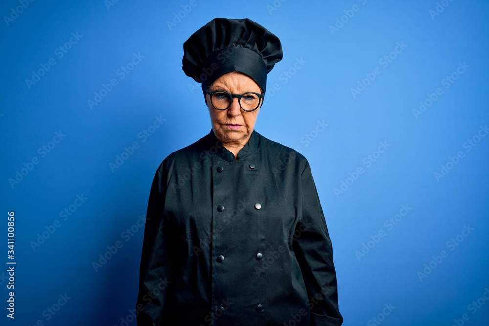 Senior beautiful grey-haired chef woman wearing cooker uniform and hat over blue background skeptic and nervous, frowning upset because of problem. Negative person. Senior beautiful grey-haired chef woman wearing cooker uniform and hat over blue background skeptic and nervous, frowning upset because of problem. Negative person.