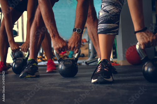 Detail of people holding a kettlebell placed on the floor of a gym