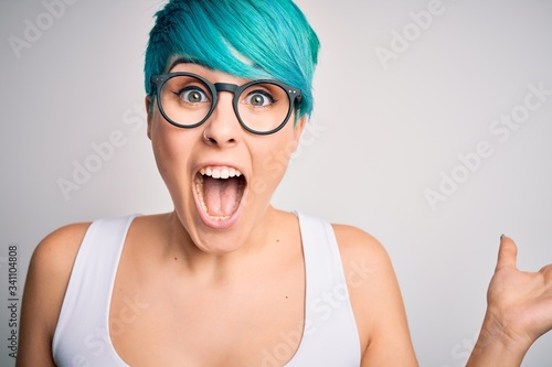 Young beautiful woman with blue fashion hair wearing casual t-shirt and glasses very happy and excited, winner expression celebrating victory screaming with big smile and raised hands