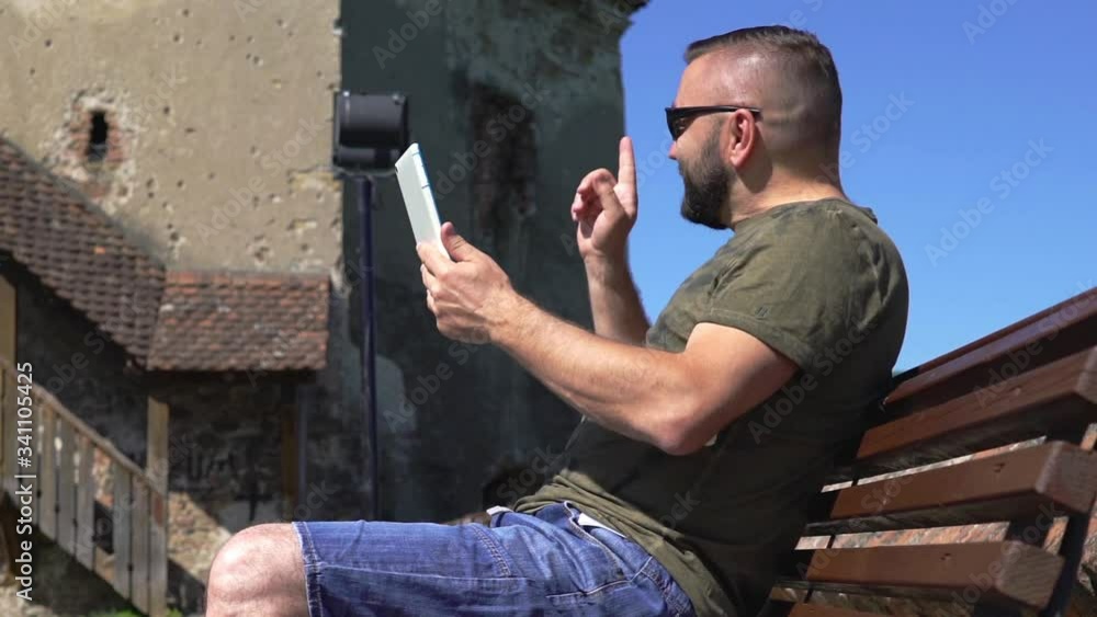 Man sitting on the bench in old town and having a videocall on tablet
Man sitting on the bench in old town and having a videocall on tablet