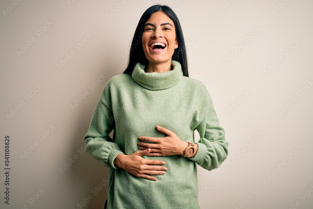 Young beautiful hispanic woman wearing green winter sweater over isolated background smiling and laughing hard out loud because funny crazy joke with hands on body. Young beautiful hispanic woman wearing green winter sweater over isolated background smiling and laughing hard out loud because funny crazy joke with hands on body.