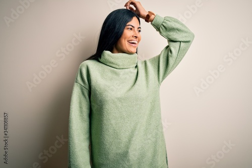 Young beautiful hispanic woman wearing green winter sweater over isolated background smiling confident touching hair with hand up gesture, posing attractive and fashionable © Krakenimages.com