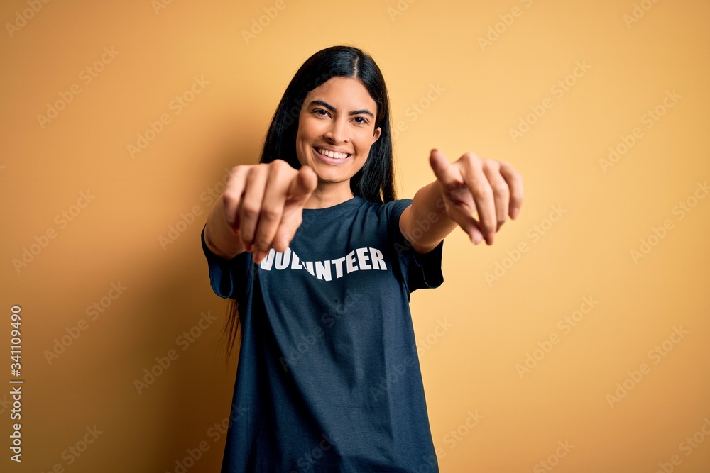 Young beautiful hispanic woman wearing volunteer t-shirt as social charity moral pointing to you and the camera with fingers, smiling positive and cheerful Young beautiful hispanic woman wearing volunteer t-shirt as social charity moral pointing to you and the camera with fingers, smiling positive and cheerful