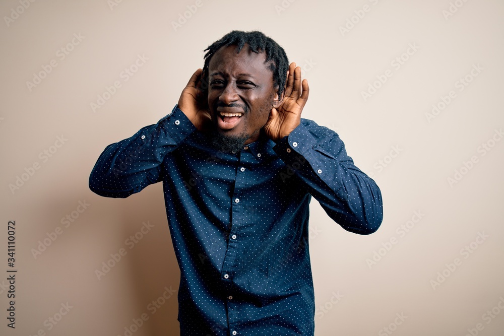 Young handsome african american man wearing casual shirt standing over white background Trying to hear both hands on ear gesture, curious for gossip. Hearing problem, deaf Young handsome african american man wearing casual shirt standing over white background Trying to hear both hands on ear gesture, curious for gossip. Hearing problem, deaf