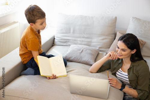 Kid getting bored while his mother working online stock photo