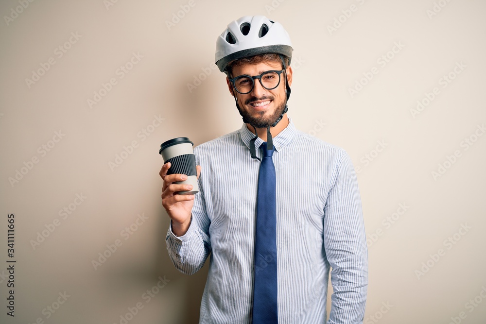 Naklejka premium Young businessman wearing glasses and bike helmet drinking cup of coffee with a happy face standing and smiling with a confident smile showing teeth