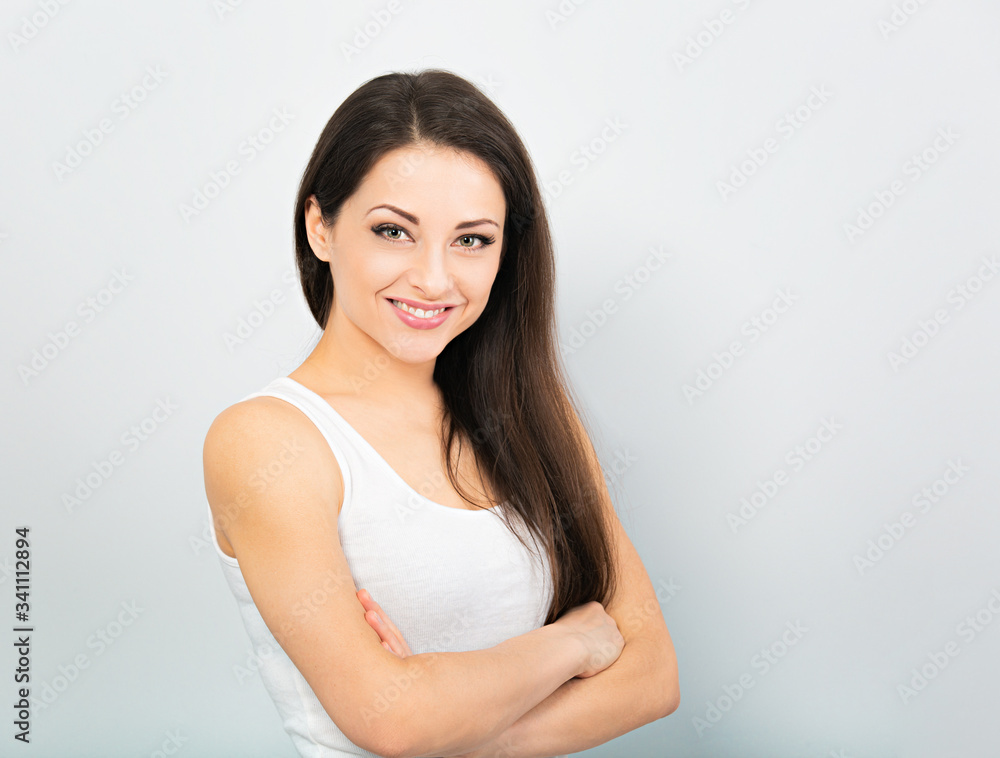 Beautiful positive young happy woman with folded arms thinking and looking in casual white t-shirt and long hair on blue background. Closeup Beautiful positive young happy woman with folded arms thinking and looking in casual white t-shirt and long hair on blue background. Closeup