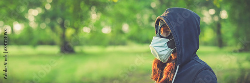 Woman wearing old hazmat style gas mask and medical mask, outside in bright summer environment.