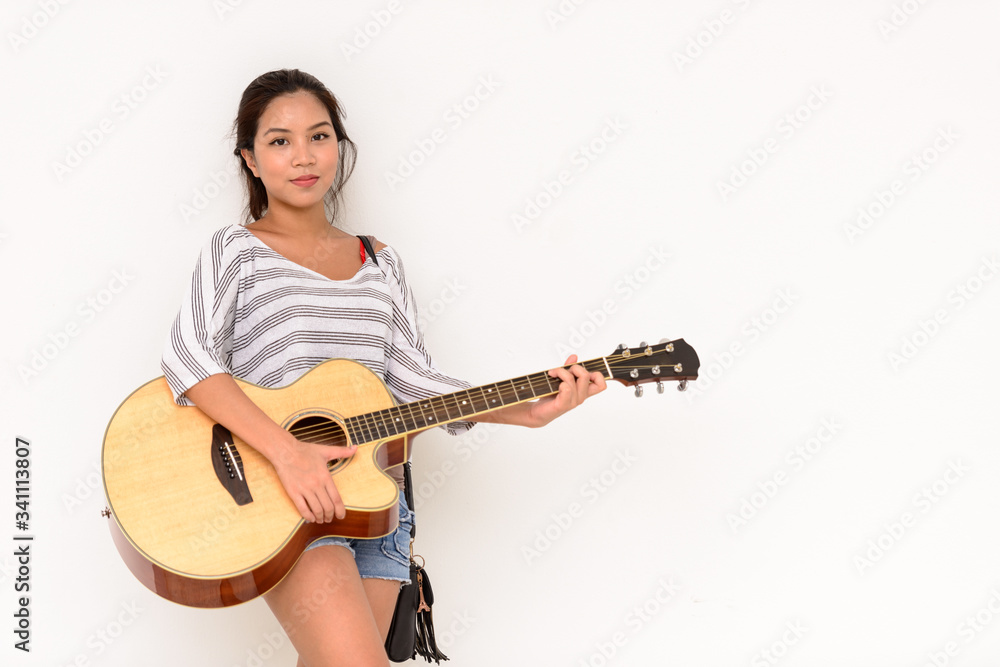 Young beautiful Asian woman playing guitar against white background Young beautiful Asian woman playing guitar against white background