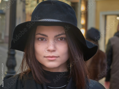 Portrait of young brown haired caucasian woman wearing black hat and coat outdoors
