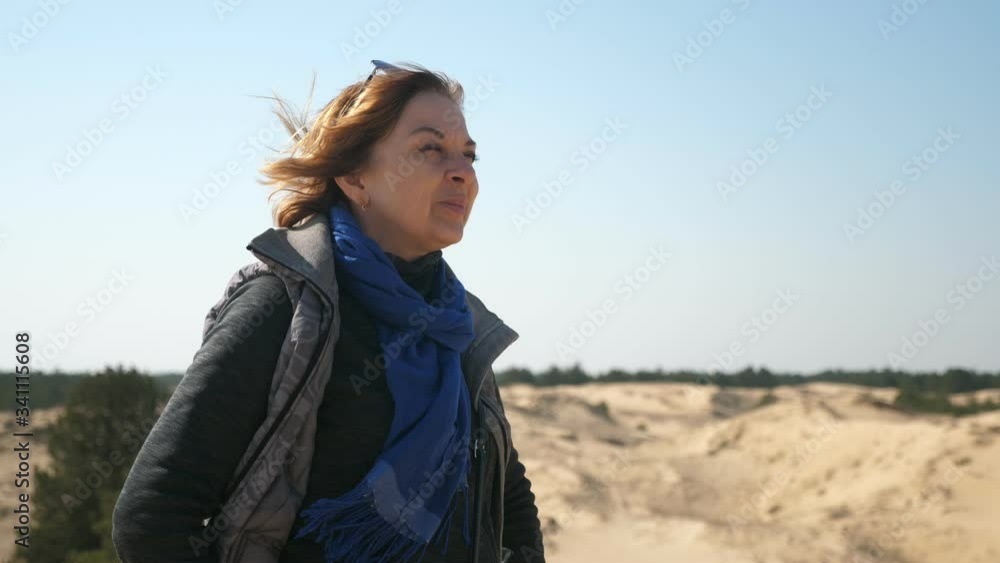 Splendid view of an optimistic female traveler in sunglasses, jeans, jacket, and scarf, standing, smiling and looking far away in dry desert on sunny day in spring Splendid view of an optimistic female traveler in sunglasses, jeans, jacket, and scarf, standing, smiling and looking far away in dry desert on sunny day in spring