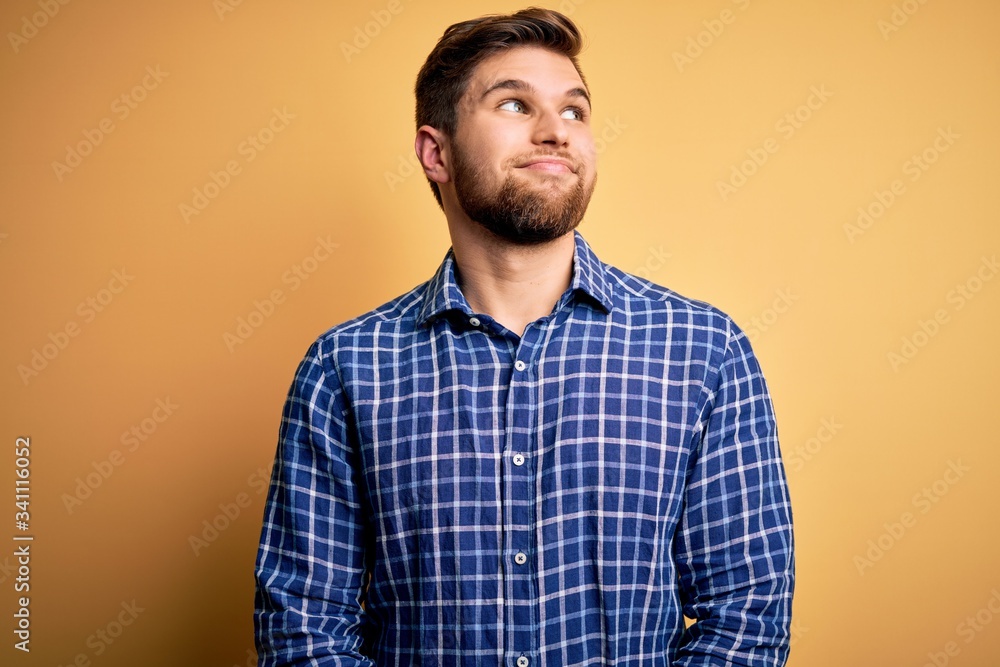 Young blond businessman with beard and blue eyes wearing shirt over yellow background smiling looking to the side and staring away thinking. Young blond businessman with beard and blue eyes wearing shirt over yellow background smiling looking to the side and staring away thinking.