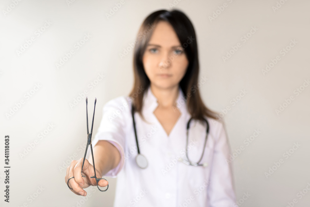 Young woman doctor with dark hair in a white medical coat, with a stethoscope and scissors. Horizontal frame Young woman doctor with dark hair in a white medical coat, with a stethoscope and scissors. Horizontal frame