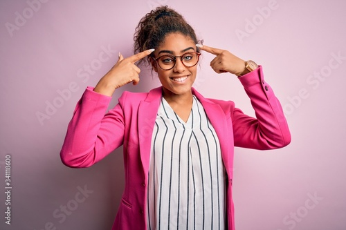 Beautiful african american businesswoman wearing jacket and glasses over pink background smiling pointing to head with both hands finger, great idea or thought, good memory © Krakenimages.com