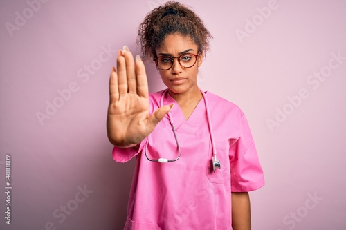 African american nurse girl wearing medical uniform and stethoscope over pink background doing stop sing with palm of the hand. Warning expression with negative and serious gesture on the face. © Krakenimages.com