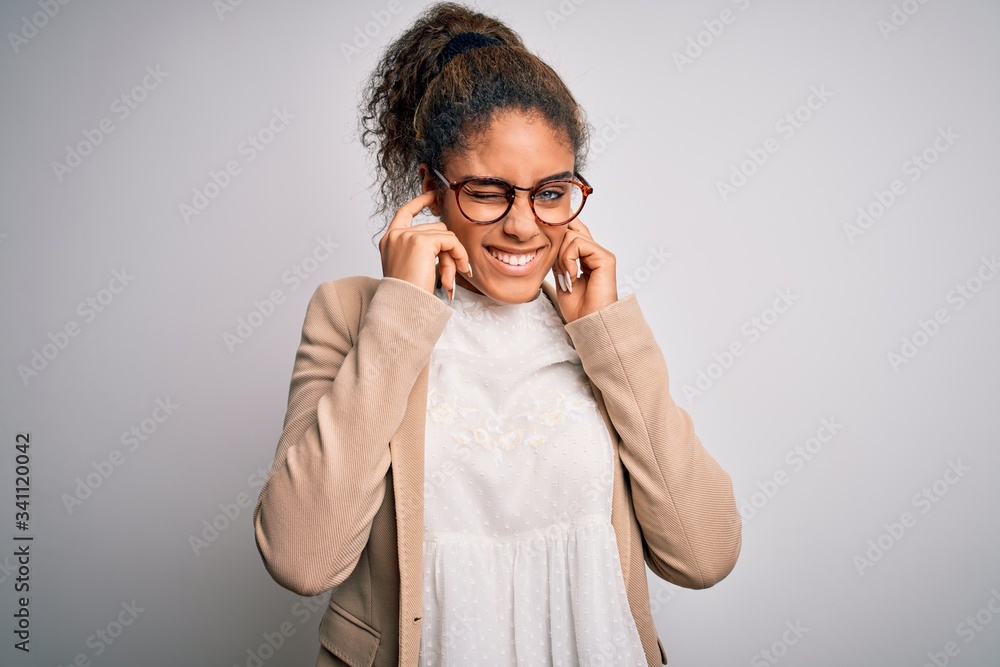 Beautiful african american businesswoman wearing jacket and glasses over white background covering ears with fingers with annoyed expression for the noise of loud music. Deaf concept. Beautiful african american businesswoman wearing jacket and glasses over white background covering ears with fingers with annoyed expression for the noise of loud music. Deaf concept.