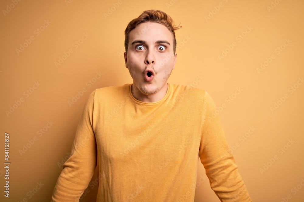 Young handsome redhead man wearing casual sweater over isolated yellow background afraid and shocked with surprise expression, fear and excited face. Young handsome redhead man wearing casual sweater over isolated yellow background afraid and shocked with surprise expression, fear and excited face.