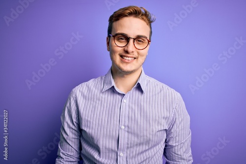 Young handsome redhead man wearing casual shirt and glasses over purple background with a happy and cool smile on face. Lucky person.