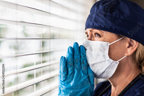 Fotografie, Obraz Prayerful Stressed Female Doctor or Nurse On Break At Window Wearing Medical Fac