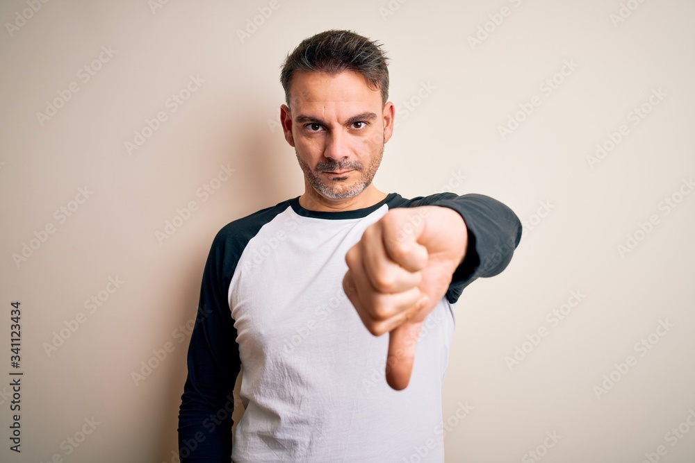 Young handsome man wearing casual t-shirt standing over isolated white background looking unhappy and angry showing rejection and negative with thumbs down gesture. Bad expression. Young handsome man wearing casual t-shirt standing over isolated white background looking unhappy and angry showing rejection and negative with thumbs down gesture. Bad expression.