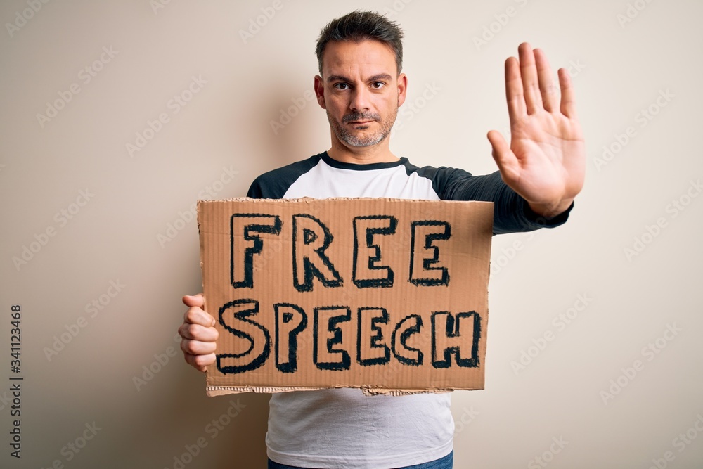 Young handsome man asking for rights holding banner with free speech message with open hand doing stop sign with serious and confident expression, defense gesture Young handsome man asking for rights holding banner with free speech message with open hand doing stop sign with serious and confident expression, defense gesture