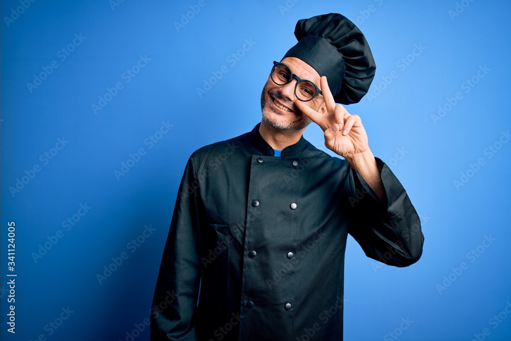 Young handsome chef man wearing cooker uniform and hat over isolated blue background Doing peace symbol with fingers over face, smiling cheerful showing victory Young handsome chef man wearing cooker uniform and hat over isolated blue background Doing peace symbol with fingers over face, smiling cheerful showing victory