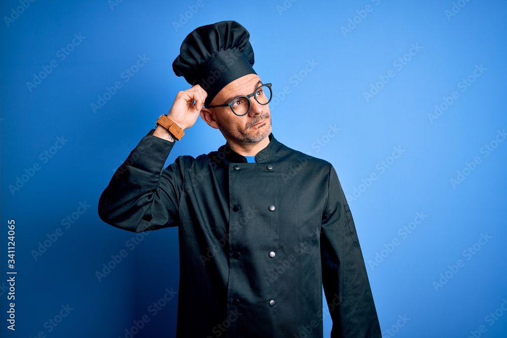 Young handsome chef man wearing cooker uniform and hat over isolated blue background confuse and wondering about question. Uncertain with doubt, thinking with hand on head. Pensive concept. Young handsome chef man wearing cooker uniform and hat over isolated blue background confuse and wondering about question. Uncertain with doubt, thinking with hand on head. Pensive concept.
