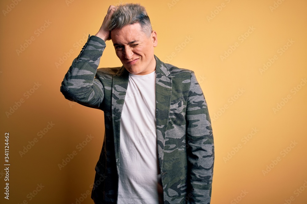 Young handsome modern man wearing business jacket standing over yellow isolated background confuse and wonder about question. Uncertain with doubt, thinking with hand on head. Pensive concept. Young handsome modern man wearing business jacket standing over yellow isolated background confuse and wonder about question. Uncertain with doubt, thinking with hand on head. Pensive concept.