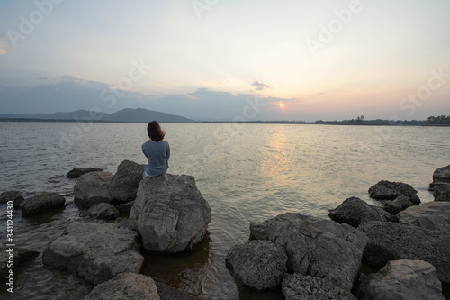 one asian woman sitting on a rock watching the sunset