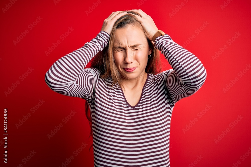 Young beautiful blonde woman wearing casual striped t-shirt over isolated red background suffering from headache desperate and stressed because pain and migraine. Hands on head. Young beautiful blonde woman wearing casual striped t-shirt over isolated red background suffering from headache desperate and stressed because pain and migraine. Hands on head.