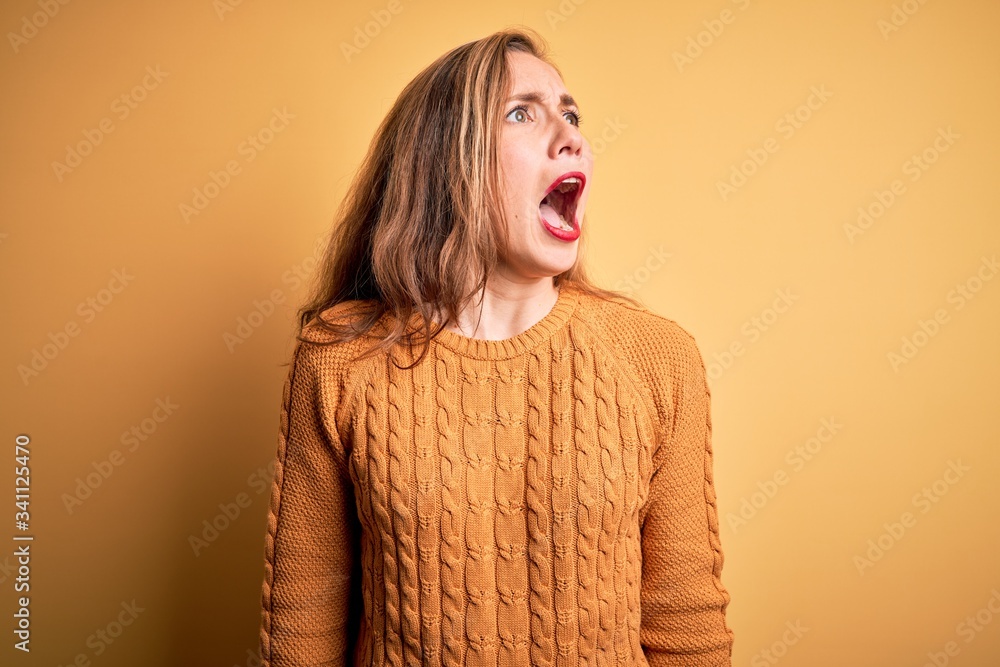 Young beautiful blonde woman wearing casual sweater standing over yellow background angry and mad screaming frustrated and furious, shouting with anger. Rage and aggressive concept. Young beautiful blonde woman wearing casual sweater standing over yellow background angry and mad screaming frustrated and furious, shouting with anger. Rage and aggressive concept.