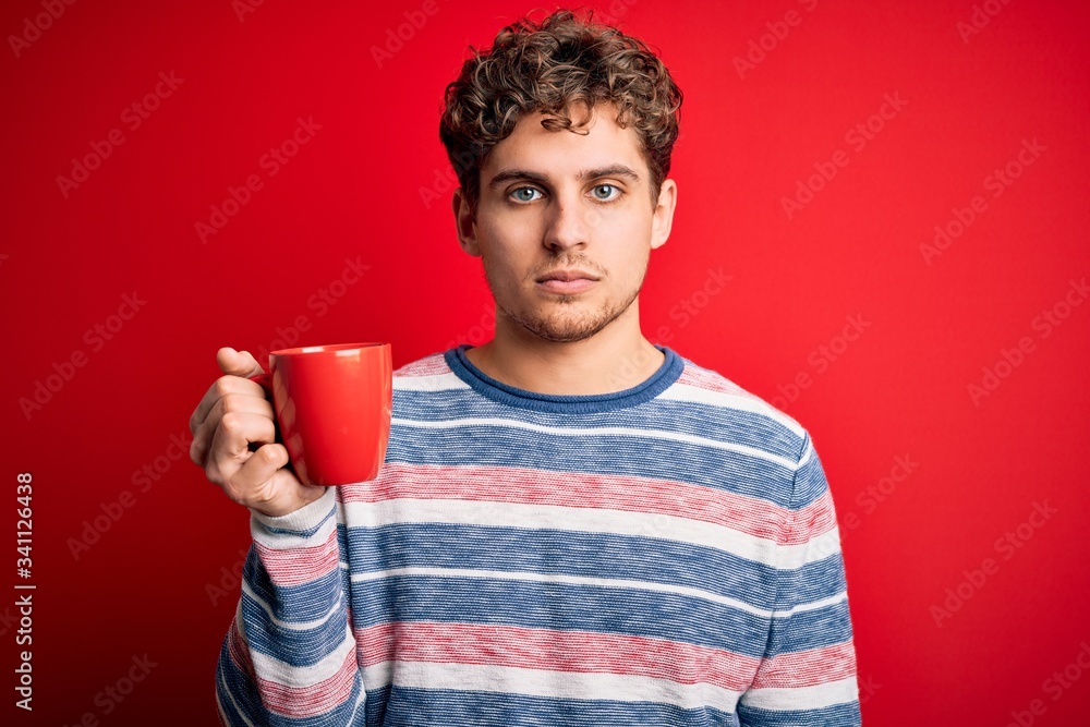 Young blond man with curly hair drinking cup of coffee standing over red background with a confident expression on smart face thinking serious Young blond man with curly hair drinking cup of coffee standing over red background with a confident expression on smart face thinking serious