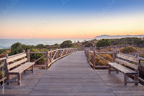 Wooden benches and walkway on Cabopino beach  Marbella  Malaga  with the sea and mountains in the background.