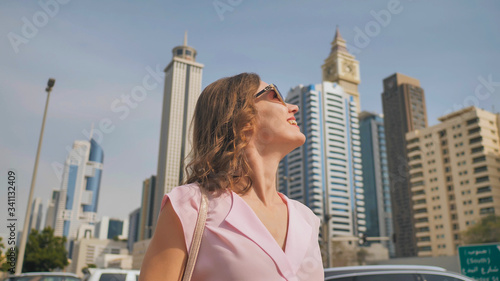 Happy girl walks in the center of Dubai against the background of skyscrapers. © Довидович Михаил
