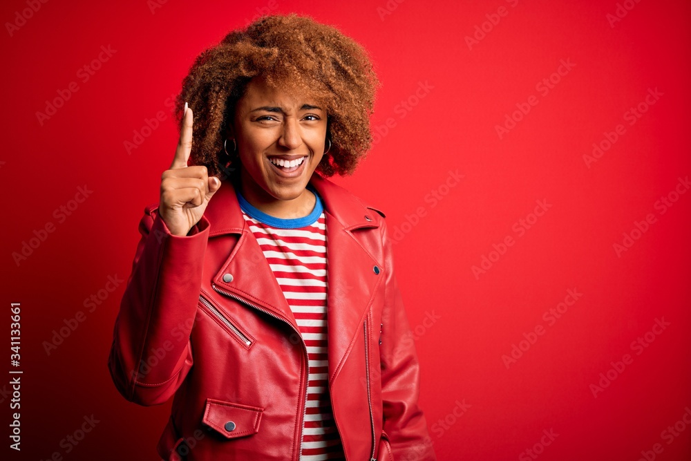 Young beautiful African American afro woman with curly hair wearing casual red jacket pointing finger up with successful idea. Exited and happy. Number one. Young beautiful African American afro woman with curly hair wearing casual red jacket pointing finger up with successful idea. Exited and happy. Number one.