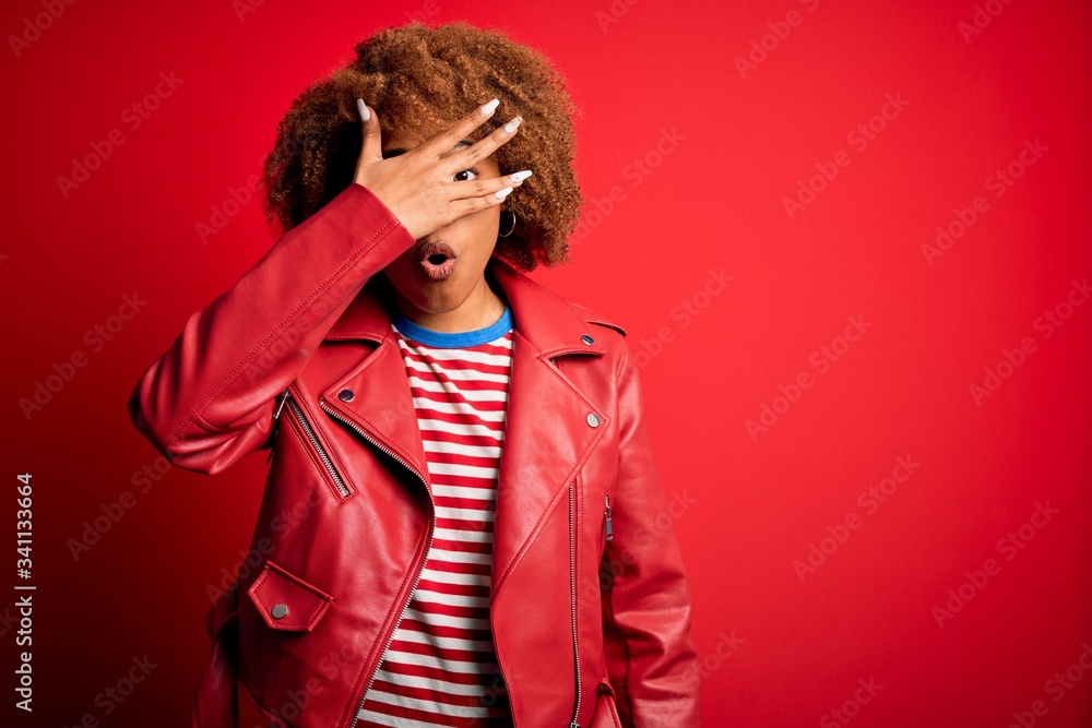 Young beautiful African American afro woman with curly hair wearing casual red jacket peeking in shock covering face and eyes with hand, looking through fingers with embarrassed expression. Young beautiful African American afro woman with curly hair wearing casual red jacket peeking in shock covering face and eyes with hand, looking through fingers with embarrassed expression.