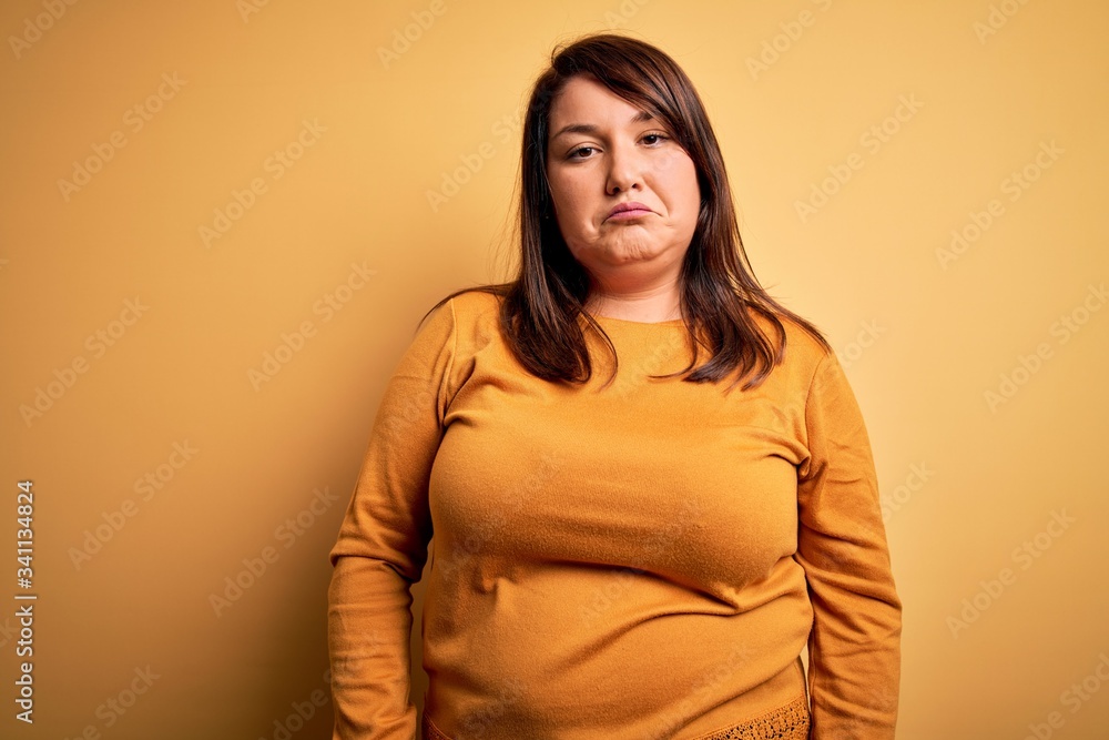 Beautiful brunette plus size woman wearing casual sweater over isolated yellow background depressed and worry for distress, crying angry and afraid. Sad expression. Beautiful brunette plus size woman wearing casual sweater over isolated yellow background depressed and worry for distress, crying angry and afraid. Sad expression.