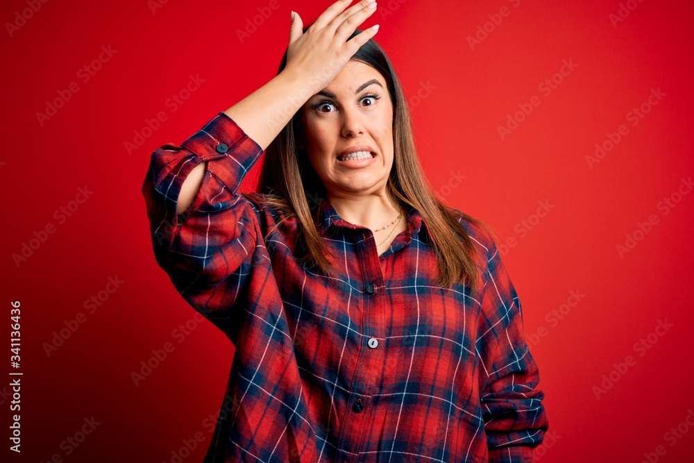 Young beautiful woman wearing casual shirt over red background surprised with hand on head for mistake, remember error. Forgot, bad memory concept. Young beautiful woman wearing casual shirt over red background surprised with hand on head for mistake, remember error. Forgot, bad memory concept.