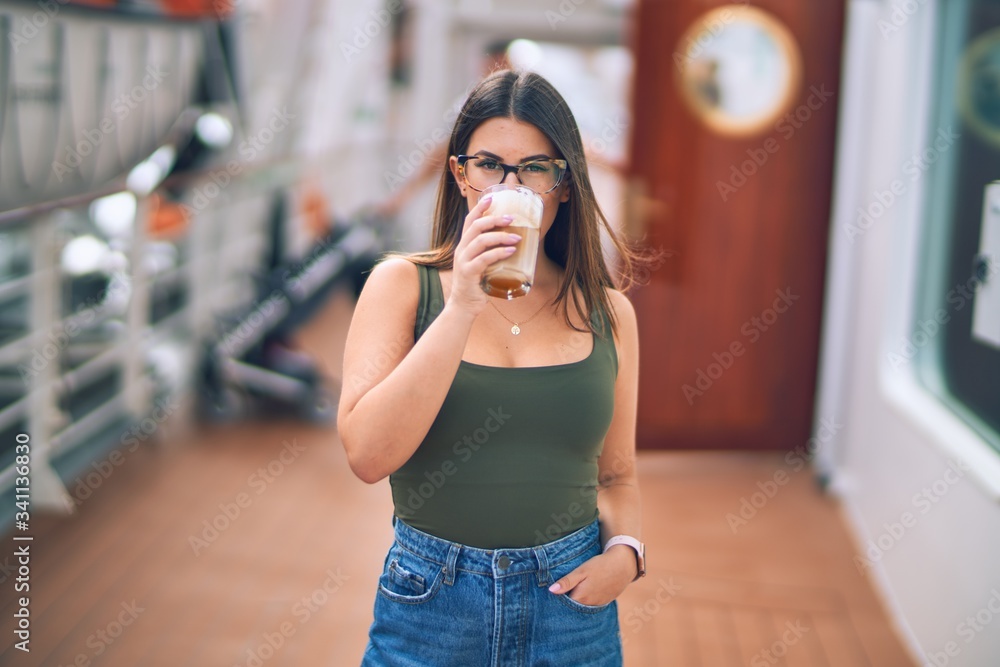Young beautiful woman on vacation smiling happy and confident. Standing on a deck of ship with smile on drinking coffee face doing a cruise